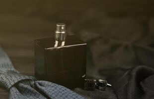 A bottle of mens cologne and cufflinks with blue tie lie on a black luxury fabric background on a wooden table. Mens accessories photo