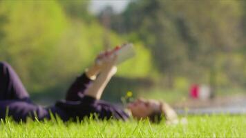 joven mujer es leyendo libro en césped en naturaleza video