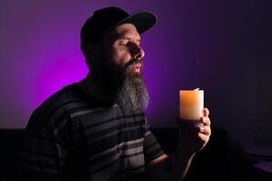 Bearded man holding a lit candle in his hand. Pink background photo