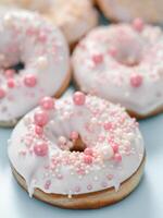 Delicious tender donuts glazed white glaze and sprinkled with pink pearl dressing. Idea decorating donuts for wedding, romantic event, celebration. Selective focus with copy space. Vertical photo