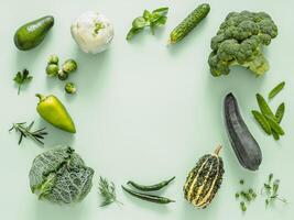 Green monochrome flat lay composition with vegetables, copy space in center. Vegetables - green peas, zucchini, avocado, bean-pod, pumpkin, broccoli, brussels sprouts, rosemary, microgreens. Top view photo