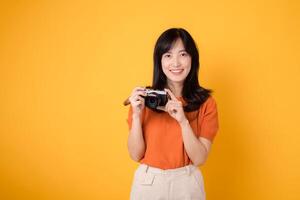 Young asian woman with a camera, ready for a fun adventure tour. Positive holiday vibes on a yellow background photo