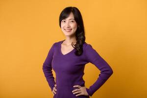 Young Asian woman in her 30s wearing purple shirt, hands on hip isolate on vibrant yellow background. wellness life advertising concept. photo