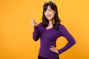 Young Asian 30s woman wearing purple shirt with happy smile showing mini heart sign isolated on yellow background, Speading love and happiness concept photo