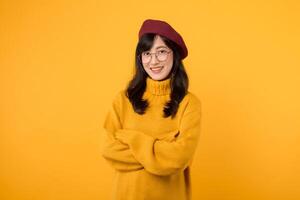 Portrait of happy asian woman 30s wearing yellow sweater shirt and red beret smiling, posing confident, cross arms on chest, standing against yellow studio background. photo