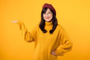 Cute Asian woman 30s with yellow shirt pointing to copy space. Pretty girl model wearing red beret and natural makeup on yellow background. photo
