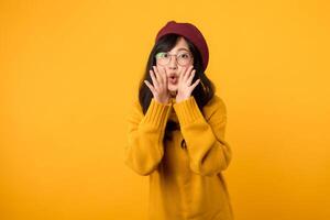 Happy young Asian woman wearing yellow sweater with open mouths raising hands screaming announcement isolated on yellow background photo