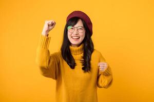 Excited young asian female wearing yellow sweater with raised hands celebrating success Portrait cheerful positive asian woman with raised hands and fists up happy, enjoy life yellow background. photo