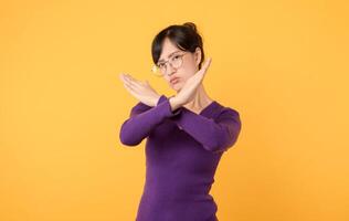 explorar concepto de negación y rechazo mediante X gesto hecho grave joven mujer vistiendo púrpura camisa y los anteojos en estudio retrato en contra un amarillo antecedentes. un impactante símbolo para precaución. foto