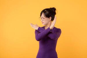 Portrait Asian beautiful young woman 30s unhappy wear purple shirt holding two cross arms say no X sign, studio shot isolated yellow background, female model pose reject gesture with copy space photo