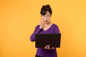 A confident and excite female entrepreneur wearing a purple shirt and eyeglasses, with a laptop, portraying a strong presence in the business world in a studio portrait against a yellow background. photo