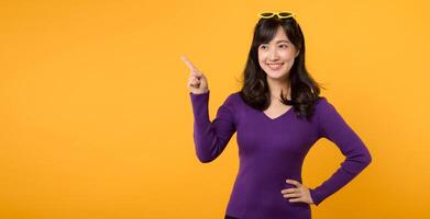 Look. Young pretty 30s asian woman wearing purple shirt expression pointing finger to free copy space for showing product isolated on yellow background. Advertisement concept. photo