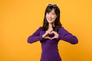 Expressing love and happiness on Valentine's Day, a cheerful young woman forms a heart shape with her hand in a studio portrait, symbolizing romance. photo