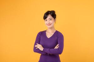 desatraillar el poder de confianza como un joven asiático mujer en su 30, poniéndose púrpura camisa, exhibiciones cruzado brazo firmar gesto en amarillo antecedentes. foto
