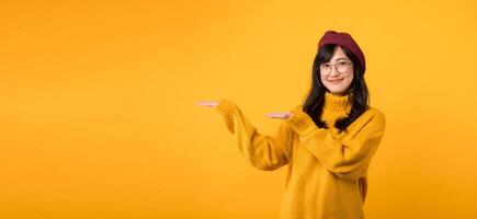 tienda con estilo como un alegre asiático mujer 30s en un amarillo suéter, rojo boina, y los anteojos puntos a viernes ofertas en contra un vibrante amarillo antecedentes. foto