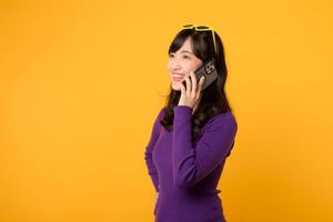 vistiendo un púrpura camisa y Gafas de sol en contra un vibrante amarillo fondo, dama con confianza usos su teléfono inteligente para en línea comunicación y negocio redes. foto