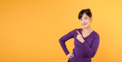 Beautiful young Asian woman 30s wearing purple shirt pointing up to copy space with smile face and happy. Pretty girl act like a satisfied product, use for advertising with yellow background photo