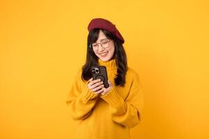 Portrait young pretty asian woman 30s wearing yellow sweater and red beret feeling happy while using smartphone explore the world. mobile application concept. photo