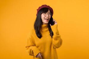 A young woman in a stylish beret and yellow sweater, chatting on her smartphone against a vibrant yellow background. photo