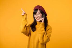 Female model in a vibrant beret and yellow sweater, pointing to free copy space on her mobile phone, set against a bright yellow background. photo