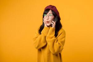 Female model in a trendy beret and yellow sweater, expressing joy while talking on her smartphone against a vibrant yellow background. photo
