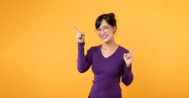 Beautiful young Asian woman 30s wearing purple shirt pointing up to copy space with smile face and happy. Pretty girl act like a satisfied product, use for advertising with yellow background photo