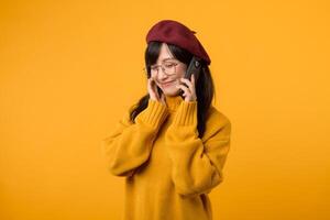 retrato joven bonito asiático mujer 30s vistiendo amarillo suéter y rojo boina sensación contento mientras utilizando teléfono inteligente explorar el mundo. móvil solicitud concepto. foto