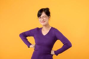 retrato joven 30s asiático mujer vistiendo púrpura camisa y los anteojos expresión alegre sonrisa mientras mano participación cadera aislado en amarillo estudio antecedentes. atractivo hembra modelo posando seguro. foto