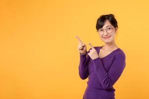 Beautiful young Asian woman 30s wearing purple shirt pointing up to copy space with smile face and happy. Pretty girl act like a satisfied product, use for advertising with yellow background photo