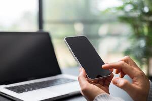 Closeup image of a woman holding and using mobile phone on wooden table in cafe. Woman play mobile game. Image of a female operating a smartphone. photo