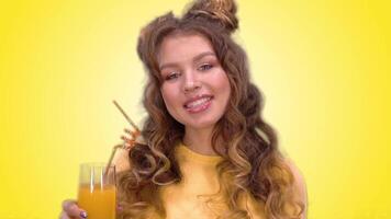 beautiful young girl in a yellow vest with a hairstyle drinking juice from a straw and smiling while looking at the camera. green screen video