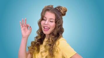 bellissimo giovane ragazza nel un' giallo veste con lungo capelli Spettacoli gesto ok strizza l'occhio e sorrisi mentre guardare in il telecamera. verde schermo video