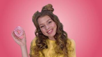 hermosa joven niña en un amarillo camisa posando con un rosquilla guiños y sonriente mientras mirando a el cámara en un rosado antecedentes. verde pantalla video