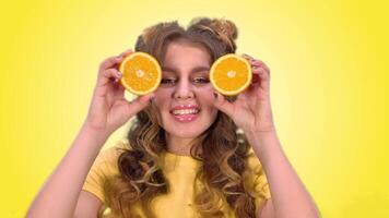 Beautiful young girl with long hair posing with oranges and smiling while looking into the camera on a yellow background. green screen video