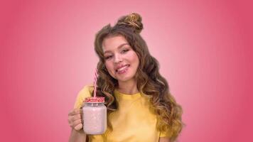 hermosa joven niña en un amarillo chaleco con peinado es Bebiendo batidos y sonriente mientras mirando a el cámara en contra un rosado antecedentes. verde pantalla video