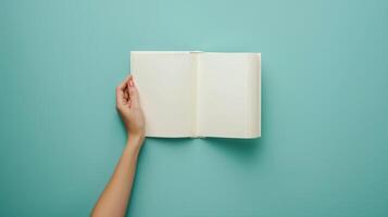 Woman hand with open empty book at light blue background. Top view. Space for text. Blank paper album mockup. photo
