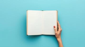 Woman hand with open empty book at light blue background. Top view. Space for text. Blank paper album mockup. photo