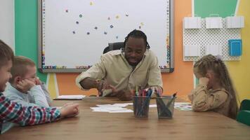 afrikanisch amerikanisch Lehrer und ein Gruppe von Kinder sind Lernen Zahlen während Sitzung beim das Tabelle im das Klassenzimmer.Schule zum Kinder, Lehren Jugendliche, dazugewinnen Wissen, lernen das Sprache. video