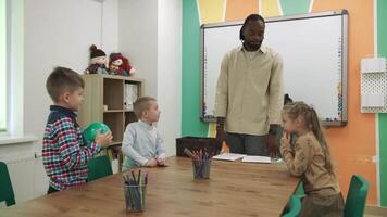 ein afrikanisch amerikanisch Lehrer unterrichtet ein Gruppe von Kinder im das Klassenzimmer im ein spielerisch Weg.Schule zum Kinder, Lehren Jugendliche, dazugewinnen Wissen, lernen das Sprache. video