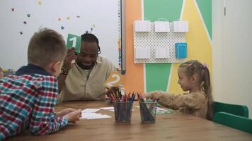 africano americano profesor y un grupo de niños son aprendizaje números mientras sentado a el mesa en el aula.escuela para niños, enseñando adolescentes, ganancia conocimiento, aprender el idioma. video