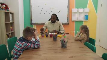 un africain américain prof et une groupe de les enfants sont en train d'étudier des fruits et animaux dans le salle de classe.école pour enfants, enseignement adolescents, Gain connaissance, apprendre le langue. video