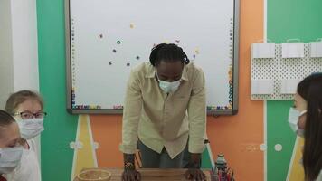 a africano americano professor ensina uma grupo do crianças às escola durante uma pandemia.escola para crianças, ensino adolescentes, ganho conhecimento, aprender a linguagem. video