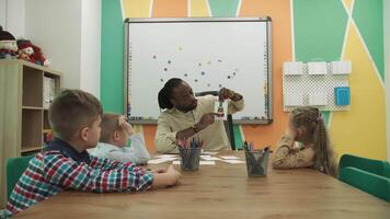 africano americano professor e alunos estude figuras enquanto sentado às a mesa dentro a sala de aula. escola para crianças, ensino adolescentes, ganho conhecimento, aprender a linguagem. video