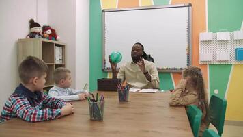 een Afrikaanse Amerikaans leraar geeft les een groep van kinderen in de klas in een speels manier.school voor kinderen, onderwijs adolescenten, krijgen kennis, leren de taal. video