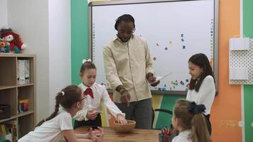 een Afrikaanse Amerikaans leraar geeft les een groep van kinderen Engels door spelen met zij.school voor kinderen, onderwijs adolescenten, krijgen kennis, leren de taal. video
