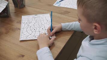 een leerling jongen verven een tekening met een gekleurde potlood terwijl zittend Bij de tafel.school voor kinderen, onderwijs adolescenten, krijgen kennis, leren de taal. video