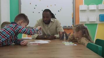 africano americano profesor y un grupo de niños son aprendizaje números mientras sentado a el mesa en el aula.escuela para niños, enseñando adolescentes, ganancia conocimiento, aprender el idioma. video