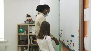 crianças dentro protetora máscaras aprender Inglês de composição palavras em uma magnético borda durante uma pandemia. escola para crianças, ensino adolescentes, ganho conhecimento, aprender a linguagem. video