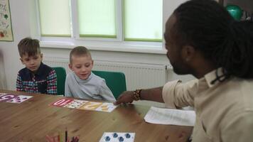 africano americano insegnante e un' gruppo di bambini siamo apprendimento numeri mentre seduta a il tavolo nel il aula.scuola per figli, insegnamento adolescenti, guadagno conoscenza, imparare il linguaggio. video