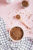 White bowl with raw whole grain buckwheat on pink background top and vertical view photo